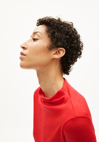 Roter Kurzarm-Top mit hohem Ausschnitt, glatter Textur und figurbetontem Design. Vor einem neutralen Hintergrund präsentiert.