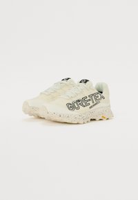 GORE-TEX idrettssko i lys gul med svart logo, teksturert såle med flekker, og sikker snøring.
