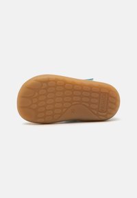 Suela de zapato con un diseño de goma texturizada; color marrón claro con patrones circulares; logo en relieve y detalles de tamaño cerca del borde.