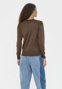 Brun stickad tröja med långa ärmar, ribbad nederdel och subtila puffade axlar, bärs över ljusblå tvåfärgade jeans, sett bakifrån.