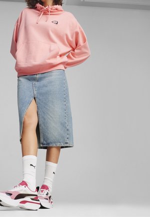 Różowa bluza z kapturem z kieszenią z przodu, zestawiona z dżinsową spódnicą o średniej długości i rozcięciem z przodu. Białe skarpetki i różowe sneakersy dopełniają stylizację.