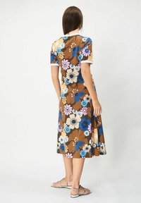 Ruskean kukkamekko, jossa on sinisiä, vaaleanpunaisia ja valkoisia kukkia, lyhyet hihat ja virtaava siluetti. Pehmeä kangas, jolla on sileä pinta.