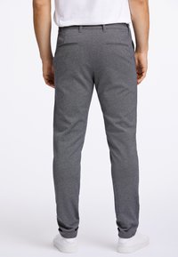 Grijze sportbroek met taps toelopend ontwerp, elastische tailleband, twee achterzakken en gestructureerde stof. Gecombineerd met witte sneakers.