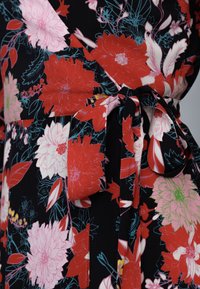 Tela de vestido floral con grandes flores rojas, rosas y verdes sobre fondo negro, cinturón de la cintura atado en un lazo.