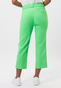 Felgroene, op maat gemaakte broek met een cropped flared leg, een gladde textuur en een achterzak. Gecombineerd met witte sportschoenen.