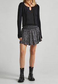 Svart ribbad kofta med volangdetaljer och knappar, kombinerad med en svart och vit mönstrad utsvängd kjol och svarta ankelstövlar.