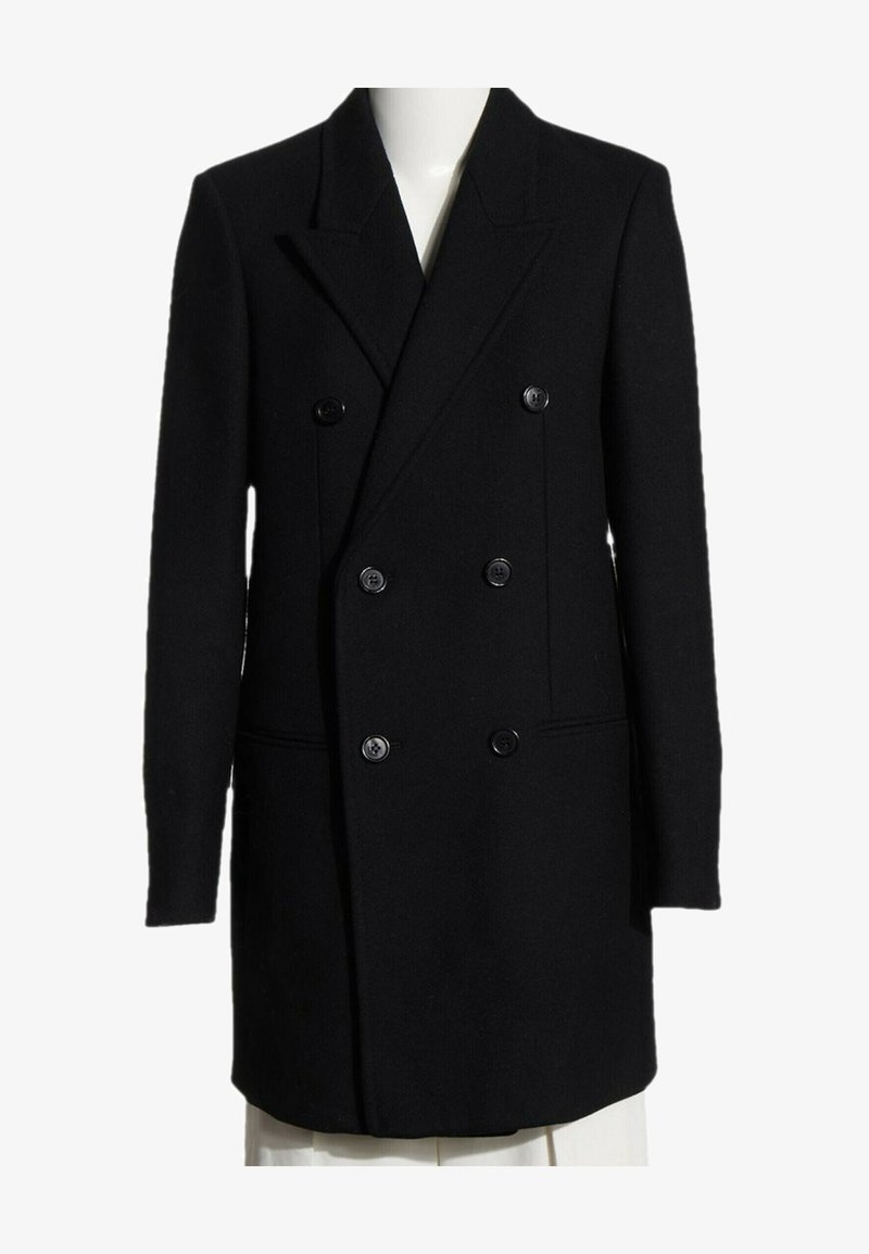 Manteau noir en laine à double boutonnage avec six boutons, revers crantés, manches longues et deux poches latérales, présenté sur un buste de mannequin blanc.