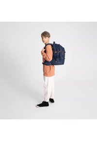 Zaino navy con motivi geometrici arancioni, spallacci regolabili, fibbie sicure e molteplici scomparti, indossato da una persona con una maglietta arancione.