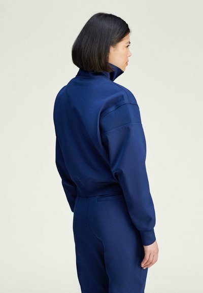 Sudadera azul marino con cuello alto, corte relajado, puños acanalados y textura suave. Representada contra un fondo neutro claro.