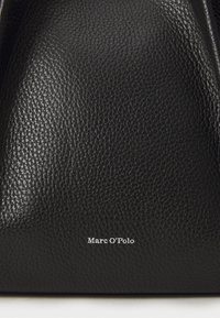 Schwarze Lederhandtasche mit strukturierter Oberfläche und silbernem Logo "Marc O'Polo", das auf der Vorderseite geprägt ist, mit einem minimalistischen Design.