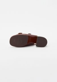 Zapato de tacón alto marrón con una suela estriada. Presenta un material exterior suave y un acento verde en el tacón.