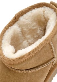 Beige Wildleder-Ankle-Boot mit einem plüschigen cremefarbenen Fellfutter, gesteppten Kanten und einem abgerundeten Kragen, der Komfort und Wärme betont.