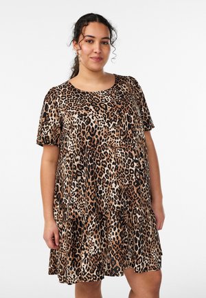 Žena s kučeravými vlasmi v krátkom šatách s leopardím vzorom po kolená na bielom pozadí.