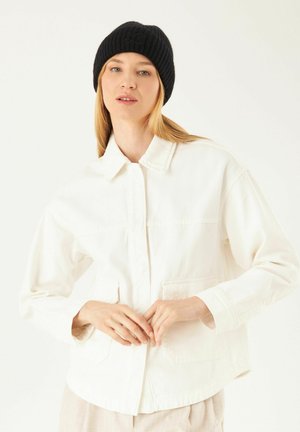 White denim jacket with a collar, long sleeves, two front pockets, and subtle texture. Model wears a black ribbed beanie.