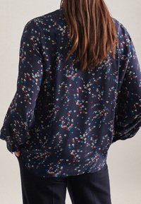 Blusa blu navy con motivi floreali in bianco, rosso e blu, con maniche lunghe e morbide e una vestibilità comoda, realizzata in tessuto leggero.