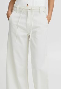 Pantalones de algodón blancos de pierna ancha con cintura ajustable, bolsillos laterales y una textura sutil. Presenta un cierre de botón en la parte delantera.