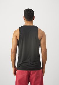 Fekete ujjatlan top, sima anyagból készült, kerek nyakkivágással és laza szabással, piros rövidnadrággal párosítva.