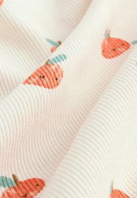 Strukturierter Stoff in Creme mit einem gerippten Muster, das gestickte orangefarbene Karotten mit grünen Blättern in einem verspielten Design zeigt.