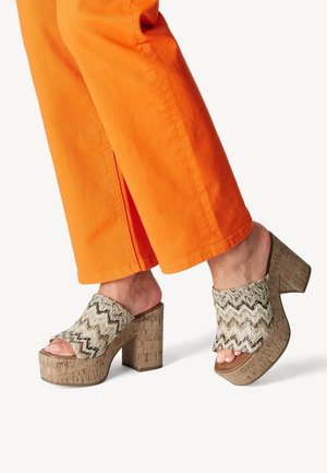 Pieds portant des sandales à plateforme à bout ouvert avec talons en liège et brides à motif zigzag, associées à un pantalon large orange vif.