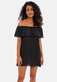 Vestido preto de ombro a ombro com bolinhas brancas, topo com babados, comprimento curto e tecido leve. Textura suave, design casual.