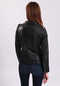 Black leather jacket with a structured fit, wide collar, quilted shoulder detail, and zipper accents on the sleeves.