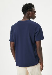 Camiseta de algodón azul marino con cuello redondo, mangas cortas y aberturas laterales, que presenta un corte relajado y una tela texturizada.