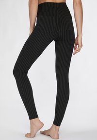 Zwarte leggings met witte verticale strepen, hoge tailleband en twee achterzakken, gemaakt van rekbaar materiaal voor comfort en pasvorm.