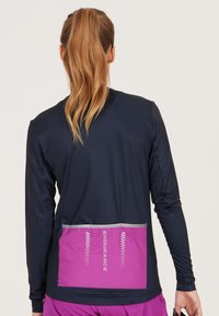 Marineblå långärmad funktionströja med en rosa reflexbakficka; slätt tyg med en kroppsnära design och kontrasterande färgpaneler.