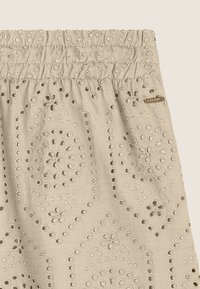 Shorts beiges brodés avec une taille froncée, présentant des motifs floraux et des découpes circulaires délicates. Des détails de petite étiquette de marque sont inclus.