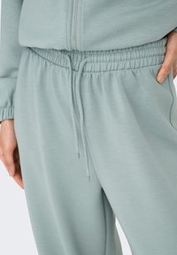 Pantalon de jogging bleu clair avec taille élastique, fermeture à cordon et tissu doux et texturé. Comprend des poches latérales et une coupe décontractée.