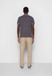 Szara koszulka polo z kołnierzykiem, w zestawieniu z beżowymi lnianymi spodniami. Koszulka ma krótkie rękawy i luźny krój.