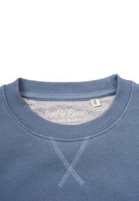 Sininen pyöreäkauluksinen collegepaita, jossa ribbikiristykset kauluksessa ja helmassa. Edessä X-ompelusyhteyskohta. Brändilappu näkyvissä kauluksen sisäpuolella.