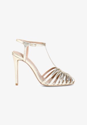 Sandale à talons hauts dorée avec des lanières, design T-strap et finition métallique élégante. Présente un talon mince et une semelle incurvée.