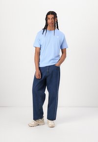 T-shirt en coton bleu clair à manches courtes, associée à un pantalon en denim bleu foncé à coupe ample et des baskets beige. Design simple, sans motifs visibles.