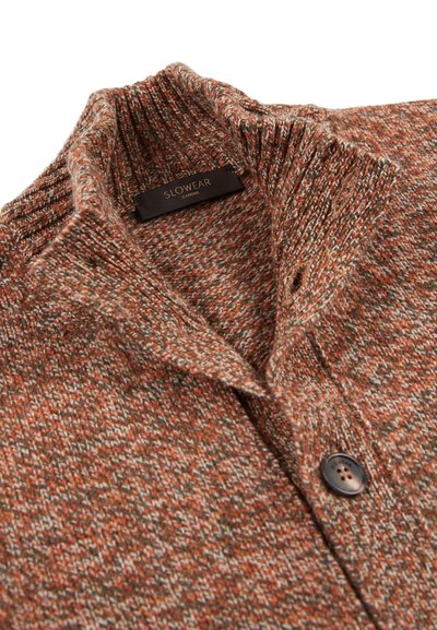 Dzianinowy kardigan w odcieniach brązowo-pomarańczowych z teksturowanym wzorem, z ściągaczem przy kołnierzu i ciemnym guzikiem z przodu. Widoczna metka marki.