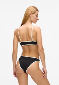 Ensemble bikini noir composé d'un crop top à fines bretelles avec un bord contrastant crème, associé à un short taille haute, tous deux en tissu doux.