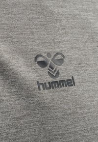 Šedý melírovaný materiál se vyznačuje hladkým povrchem. Logo "hummel" je vytištěno v tmavším odstínu, doplněné o motiv včely a chevron.
