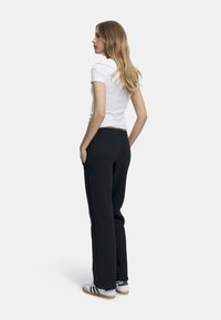 Svarte joggebukser med avslappet passform, sidelommer og elastisk liv, kombinert med en enkel hvit tettsittende t-skjorte og hvite sneakers.