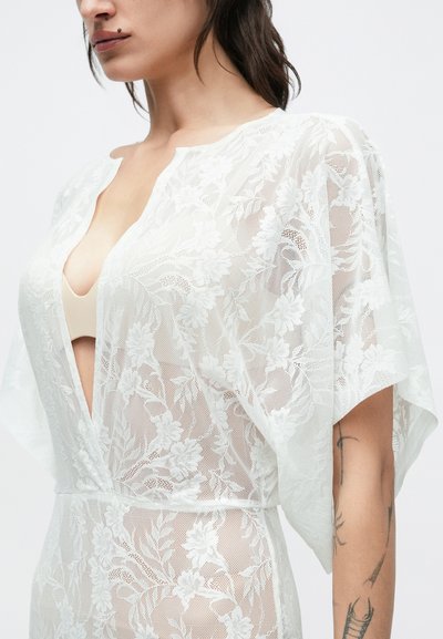 Õhuke valge pitsist kimonoga lillemustriga, esiküljelt avatud ja lühikeste varrukatega. Sile tekstuur, lõdvestunud lõige ja peened disainielemendid.
