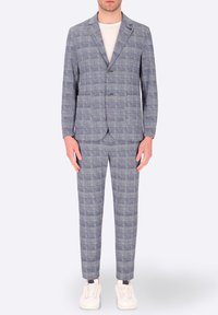 Completo a quadri grigio con una finitura testurizzata, caratterizzato da un giacca a un bottone, due tasche e pantaloni slim-fit, abbinato a sneakers bianche.