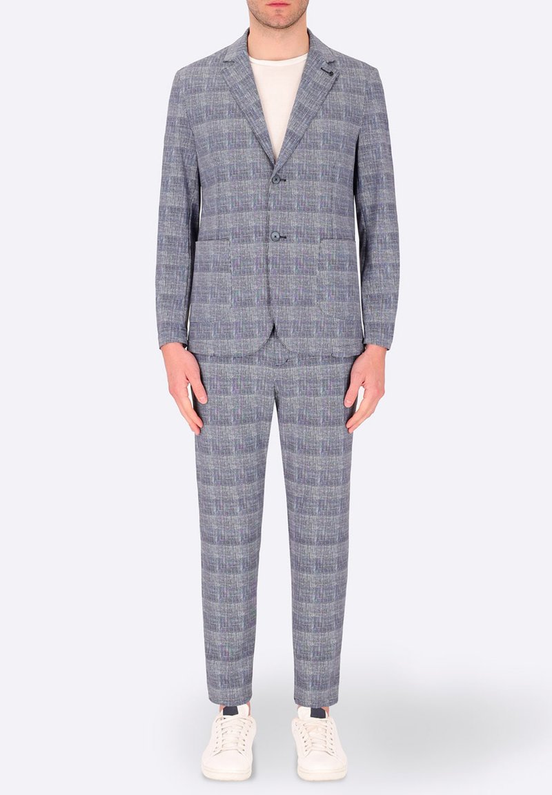 Completo a quadri grigio con una finitura testurizzata, caratterizzato da un giacca a un bottone, due tasche e pantaloni slim-fit, abbinato a sneakers bianche.
