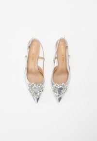 Zapatos de tacón slingback plateados con puntera afilada y embellishments de joyas en la punta, parte superior de cuero y correa ajustable al tobillo. Textura suave.