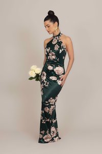 Grünes Satin-Halterkleid mit floralem Muster in Rosa und Weiß, tailliert, bodenlang, getragen mit goldenen Ohrringen, während sie weiße Rosen hält.