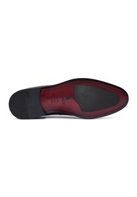 Semelle de chaussure en cuir noir avec un accent rouge, présentant une texture lisse, un motif de grip en caoutchouc et un logo de marque en relief.