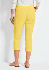 Geel cropped broek met een gladde textuur, voorzien van zijsplitten aan de zoom en een getailleerde pasvorm. Gecombineerd met een eenvoudig wit topje en sandalen.