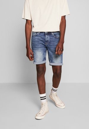 Shorts en jean à délavage bleu clair, avec revers, design classique à cinq poches, associés à un t-shirt beige et des baskets montantes.