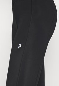 Leggings noirs en tissu extensible, avec une coupe ajustée, des coutures plates et un petit logo blanc sur le côté inférieur.