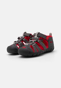 Szare i czerwone buty wodne z gumową podeszwą, siateczkową cholewką, elastycznymi sznurówkami i regulowanymi paskami dla pewnego dopasowania. Oddychająca konstrukcja z wycięciami.