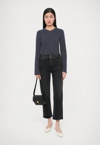 Top de manga comprida escuro com nervuras, jeans pretos de cintura subida com um cinto com tachas e sapatos brancos de bico pontudo. Mala preta com detalhes dourados.