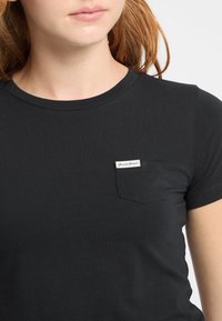 Čierne tričko s krátkym rukávom vyrobené z jemnej látky, s malou kapsičkou na ľavej hrudi s bielou nálepkou "Guess Jeans."
